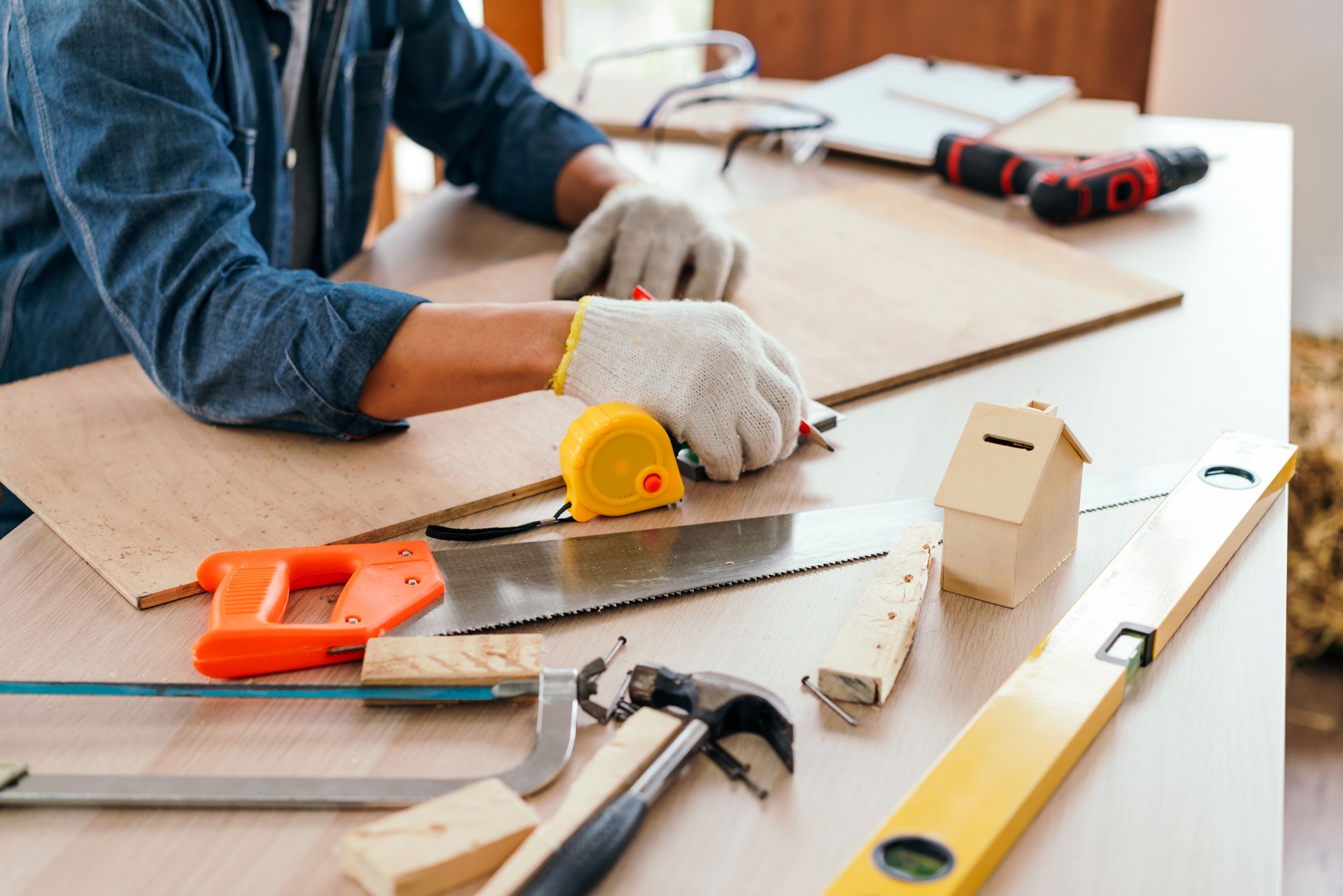 Close-up carpenter hands wearing work gloves draw the cutting line with a pencil on a wooden board. Construction industry, carpentry workshop. Carpenter at work on wooden boards. Carpentry concept.